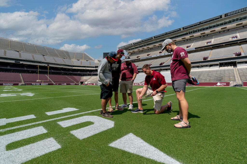 several people standing on Kyle Field and inspecting the turf