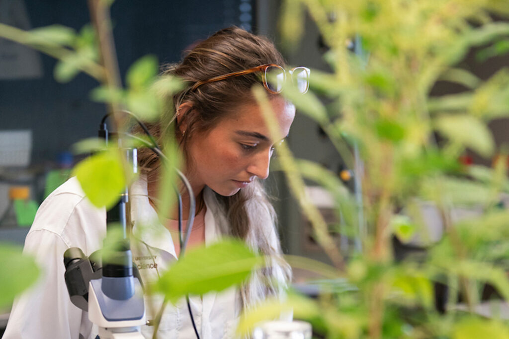 woman standing next to microscope and behind plants