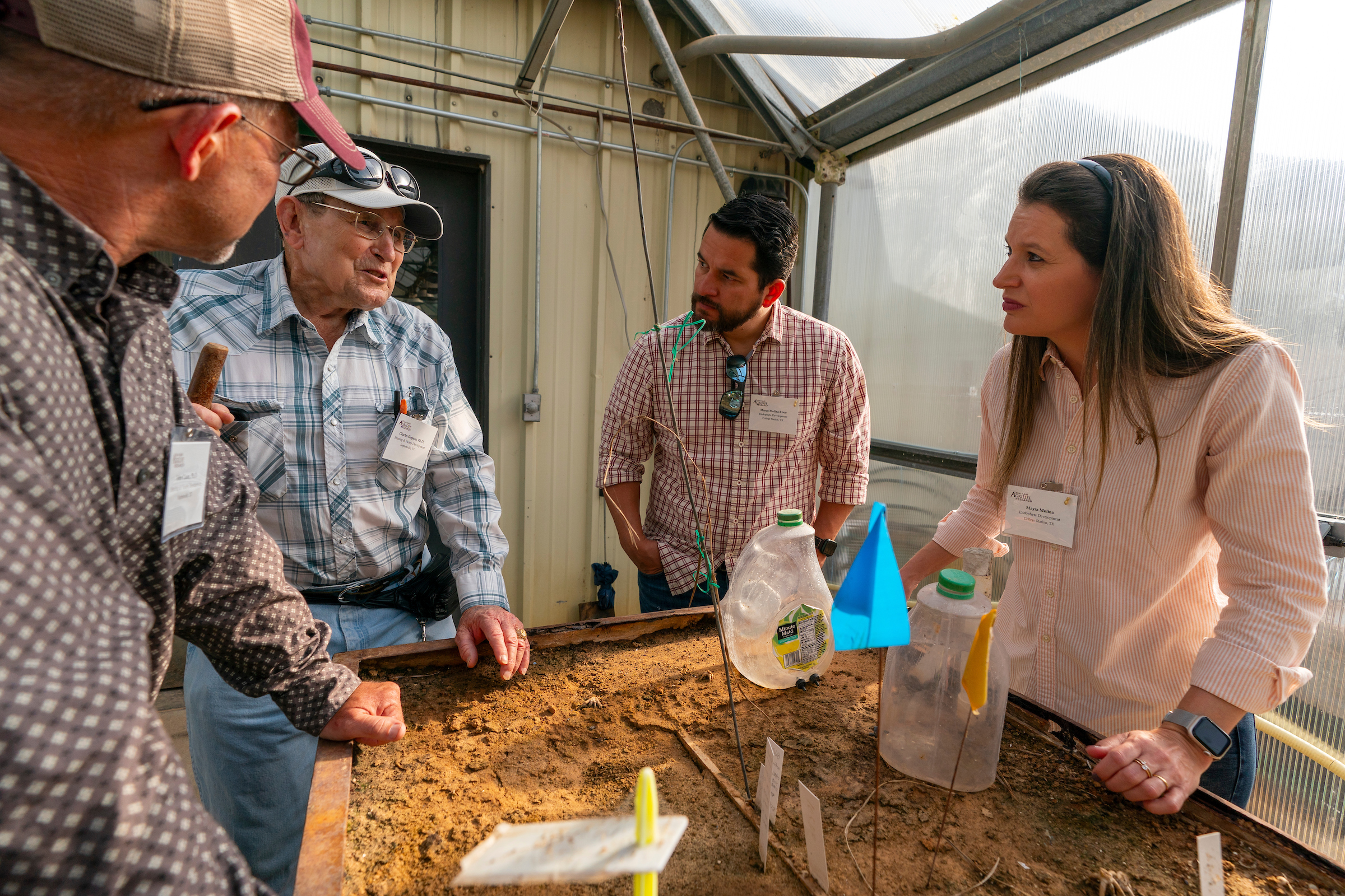 Four people standing next to a table filled with dirt. One of the men are talking while the rest listen