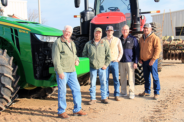 Five men stand in front of big farm equipment vehicles