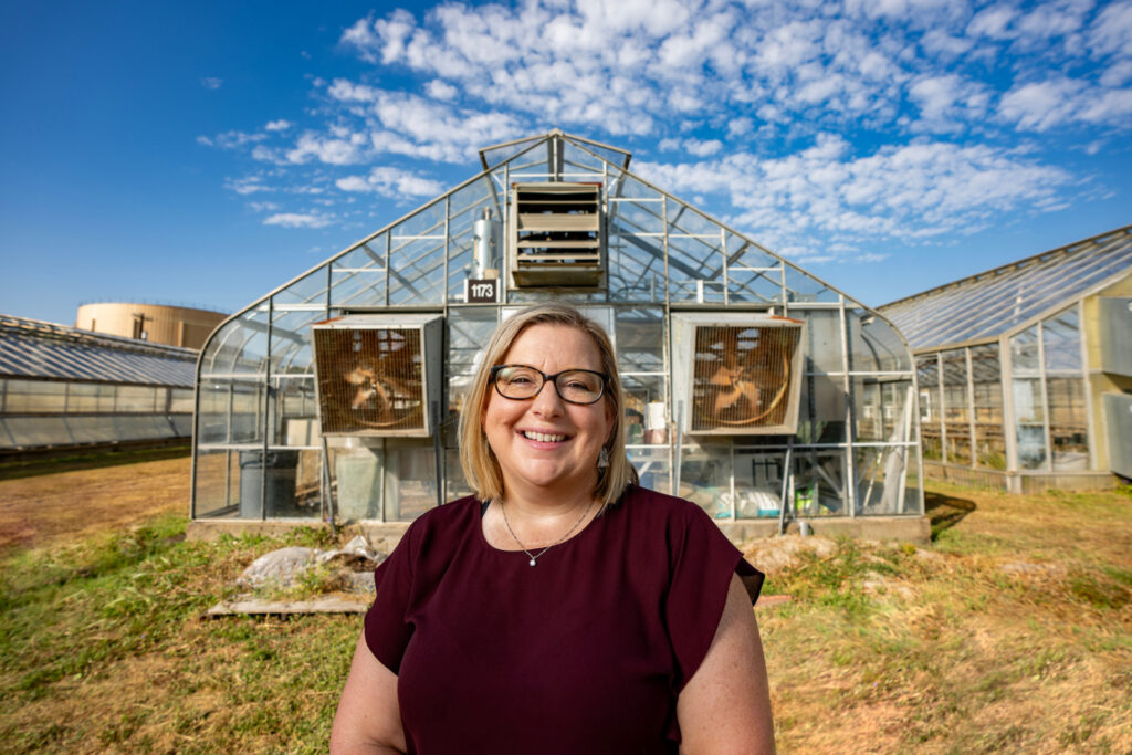 Julie Howe '95 '99, standing in front of a row of greenhouses
