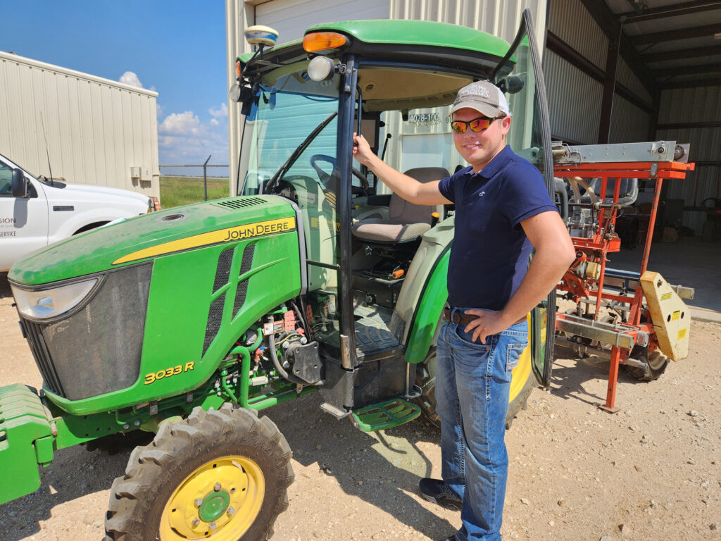 Brandon Gerrish, Ph.D., standing next to a John Deere tractor
