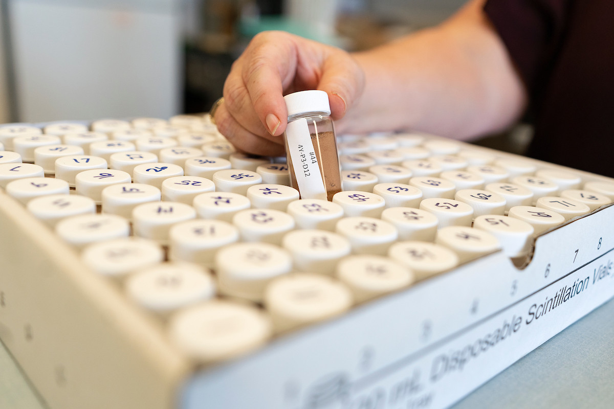 Someone takes a vial out of a box of vials containing soil samples