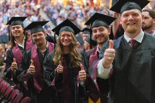 Aggies in graduation gowns posing with Gig 'Em thumbs