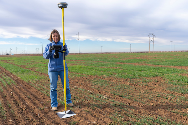 Woman standing in the middle of a crop field holding a soil analyzing device