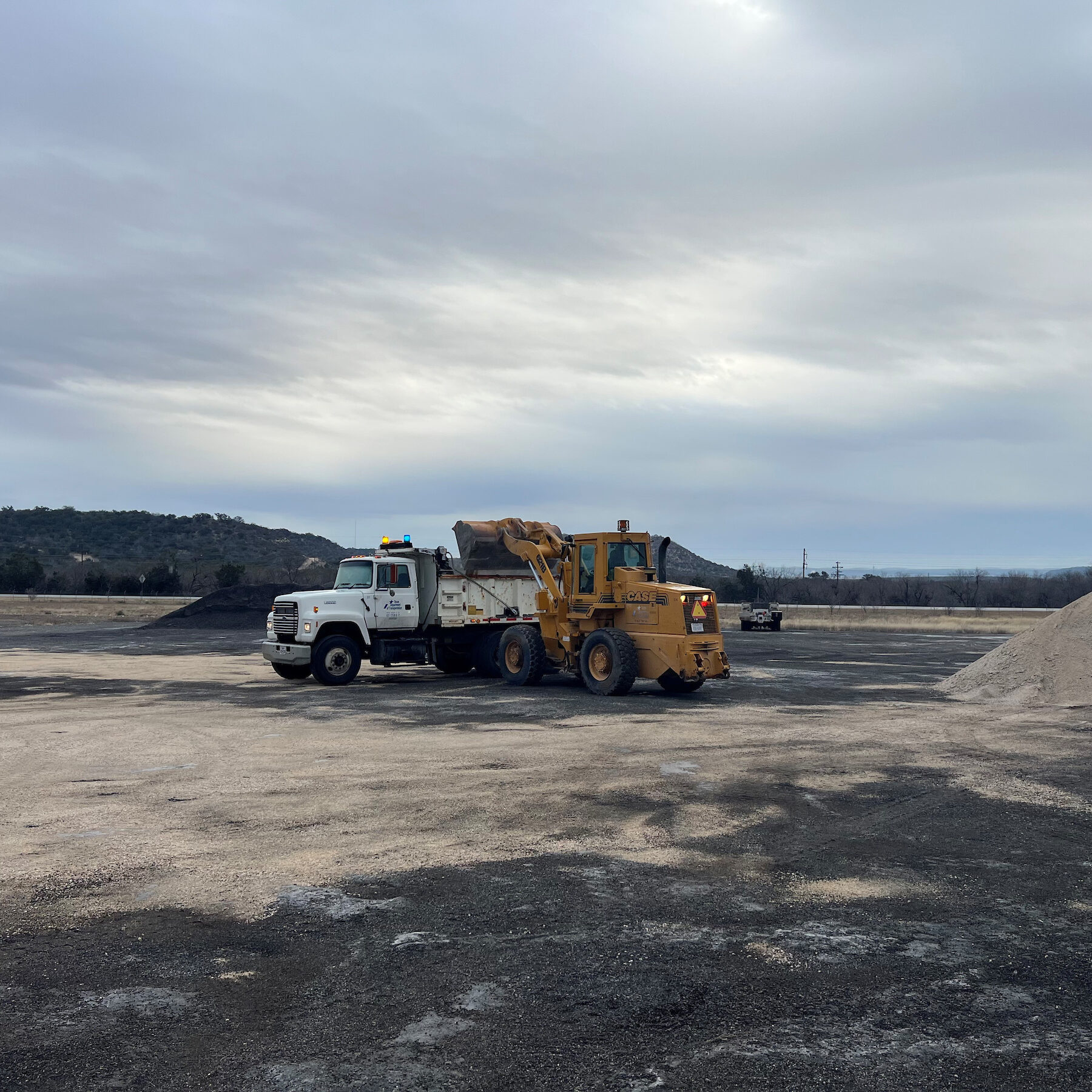 A skid steer loader dumps dirt in a dump truck